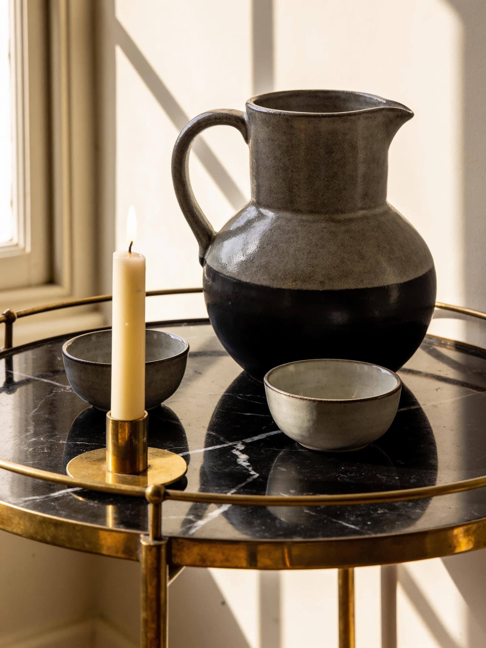 A stoneware jug, ceramic bowls and a lit taper candle