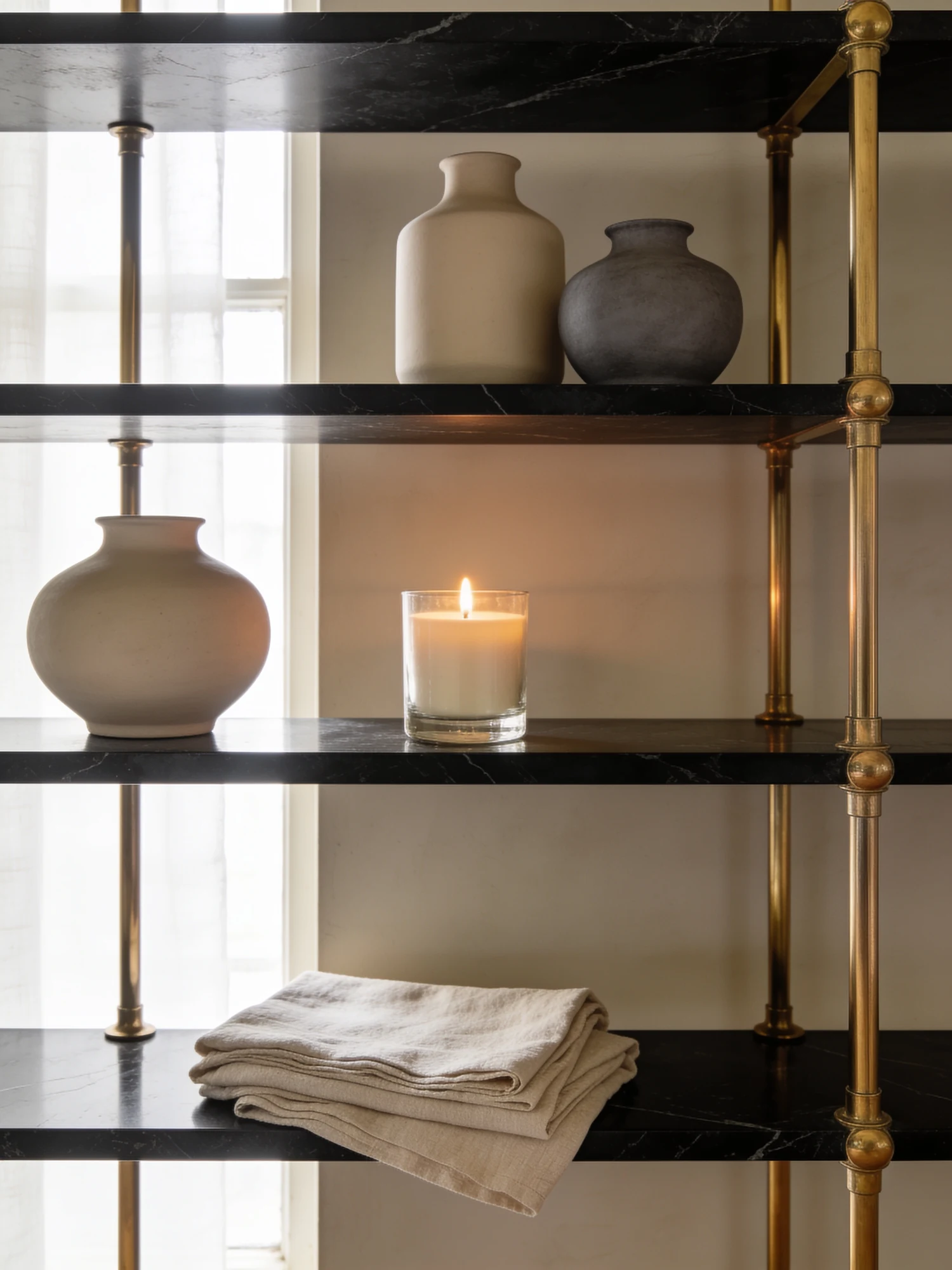 Stoneware vases, a lit candle and folded linen on a black marble shelf
